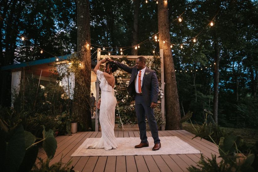 groom twirls bride on wooden platform surrounded by twinkle lights and trees