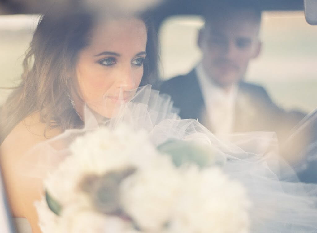 A photograph of a bride with a groom out of focus in the background.